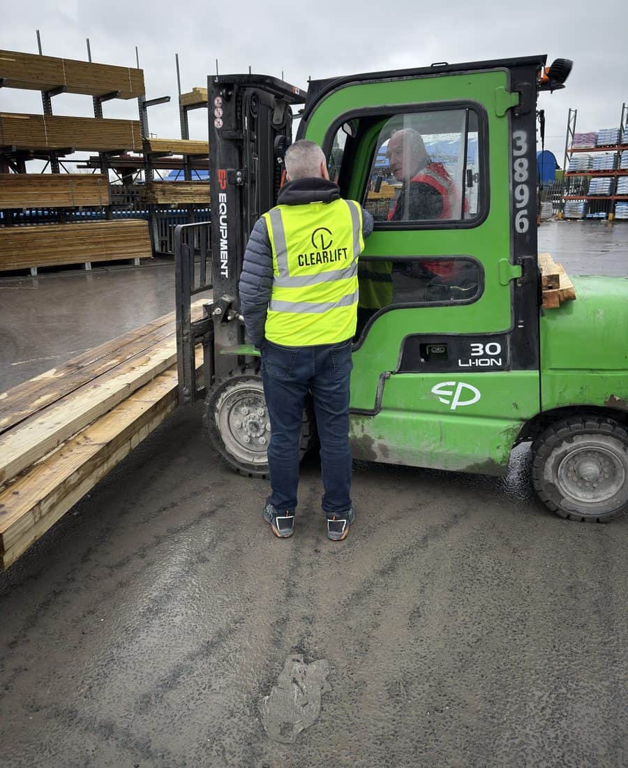 Clearlift staff member beside a green EP 3-tonne lithium-ion cab forklift with timber in a builders' yard