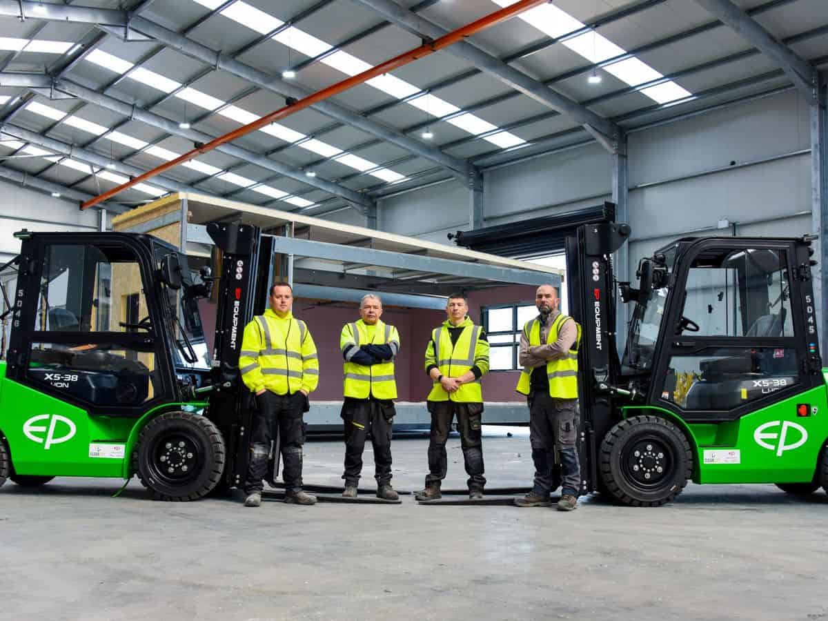 Clearlift team in hi-vis between two green EP cab forklifts in a large new warehouse