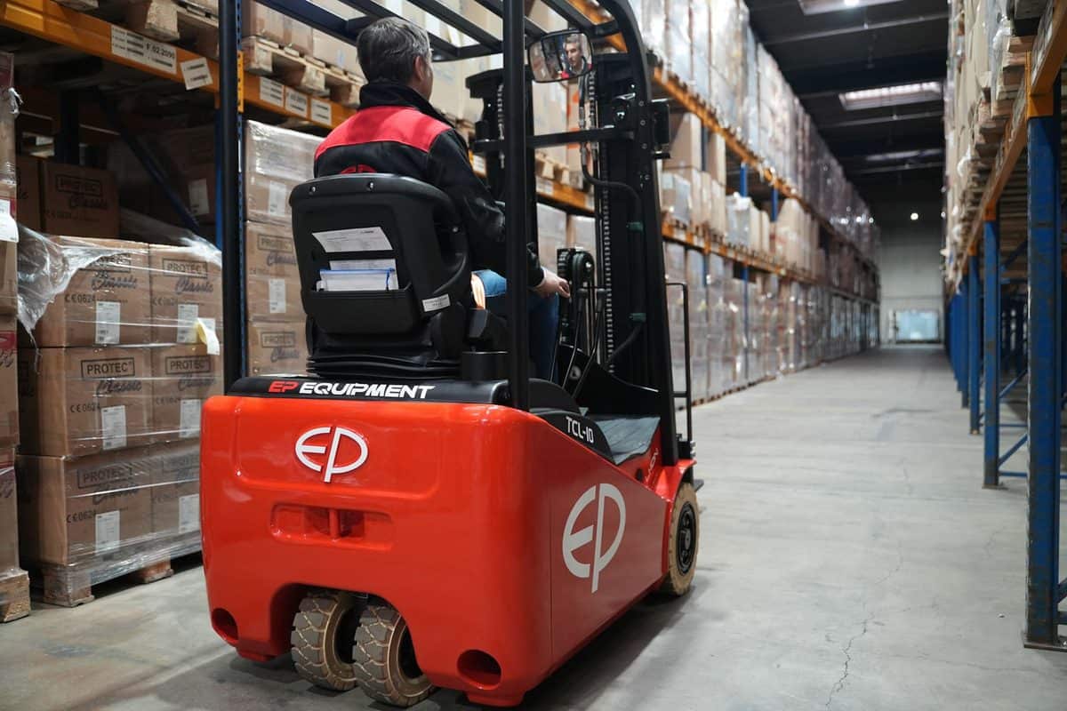 Operator driving an EP 3-wheel electric forklift down a long warehouse aisle