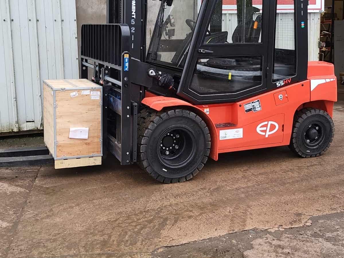 Red EP electric cab forklift carrying a wooden crate outside a manufacturing unit