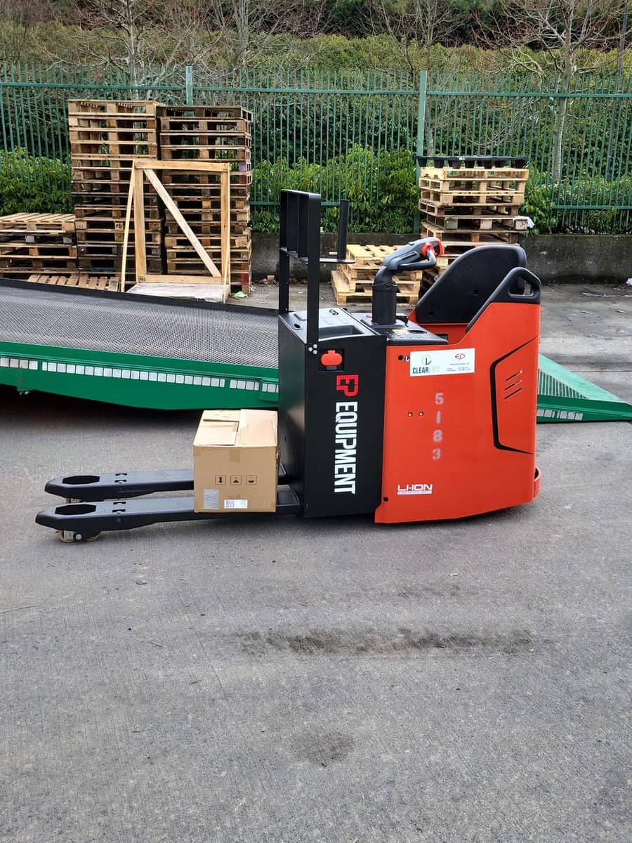 Red EP ride-on pallet truck beside a loading ramp with pallets stacked behind